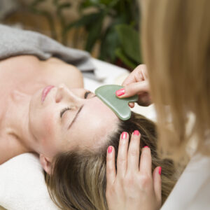 Woman having a gua sha facial massage with natural jade stone